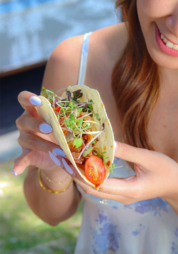 A woman holds a taco and she is smiling.