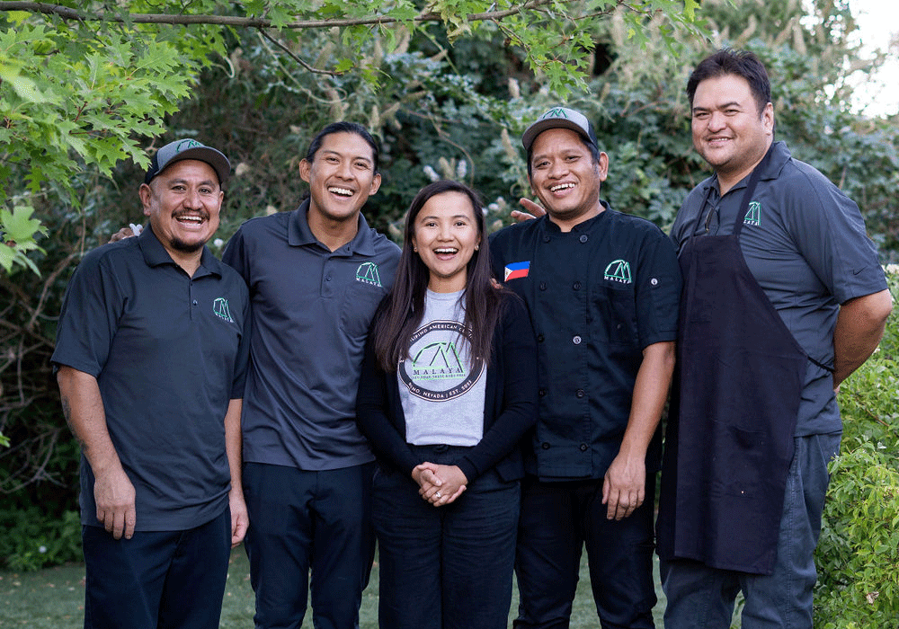 Malaya Eats' team smiling and standing in front a background of lush trees They are posed together in their Malaya Eats uniforms.